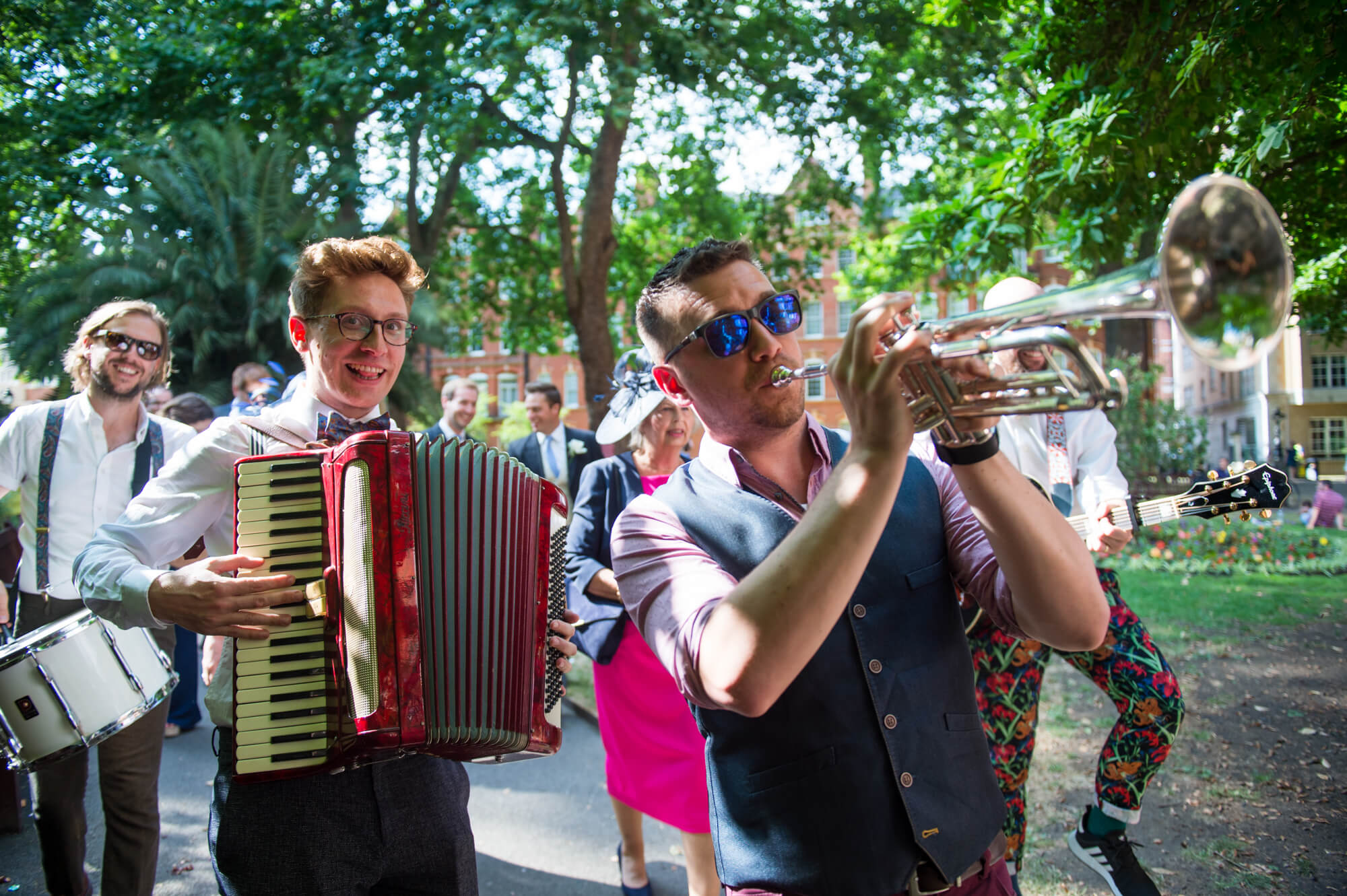 Felix Hagan playing music and leading a wedding party through a park in Mayfair